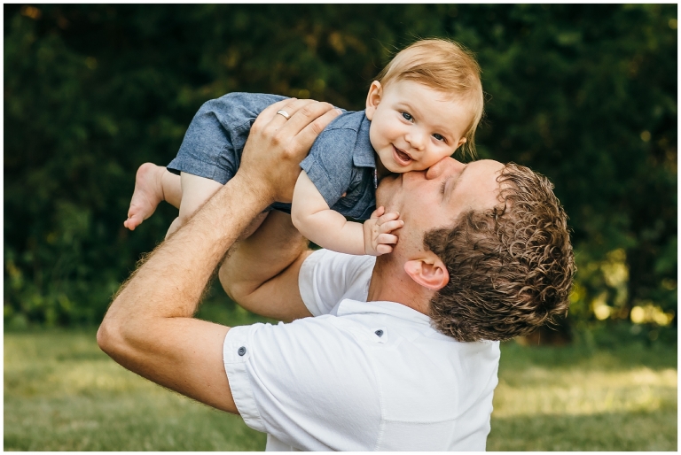 Little boy getting kissed by dad, feet in the air.